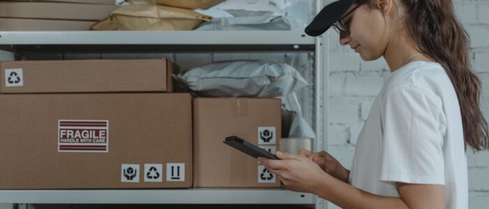 A female courier in uniform managing packages with a device in a storage room.